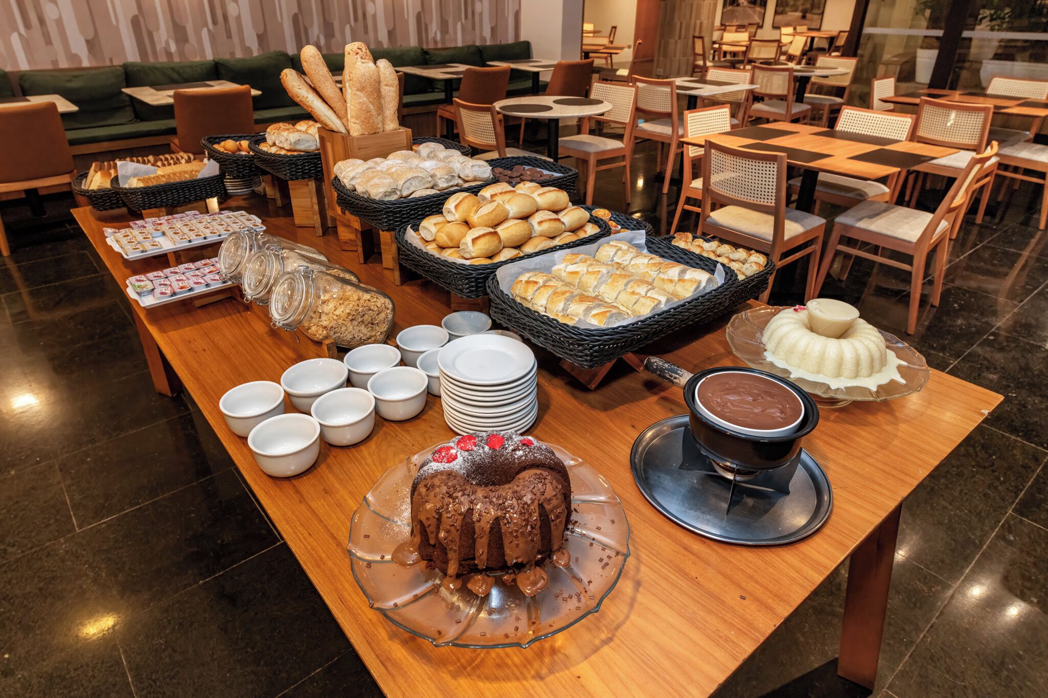A buffet table with various breads, pastries, and a chocolate cake.