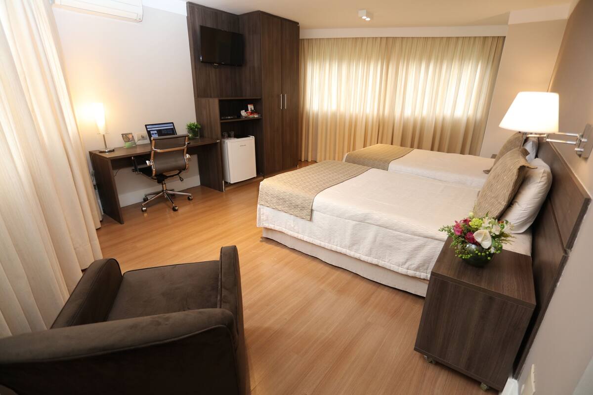Une chambre d’hôtel comprenant un lit, un bureau avec un ordinateur, une chaise, une télévision et une table de chevet avec une lampe.