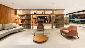 Een modern interieur met een bank, twee fauteuils, een glazen salontafel en houten planken.