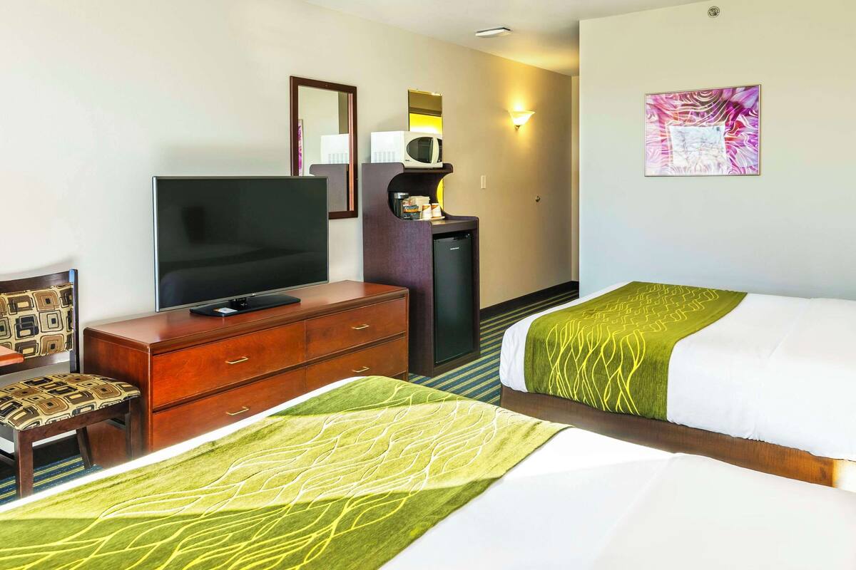 Una camera d'albergo con due letti, una TV, un minibar e uno specchio.