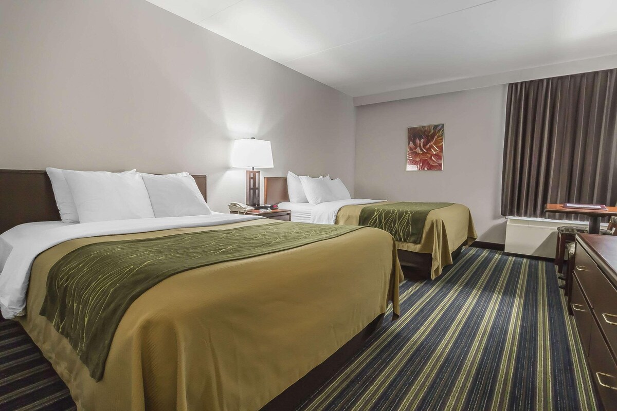 A hotel room with two beds, a desk, a chair, a lamp, and a painting on the wall.