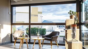 A modern room with large windows, a leather chair, a wooden table, and a potted plant. - B&B HOTEL Grenoble Centre Verlaine (Grenoble)