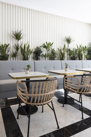 A modern indoor seating area with cushioned sofas and tables, surrounded by potted plants.