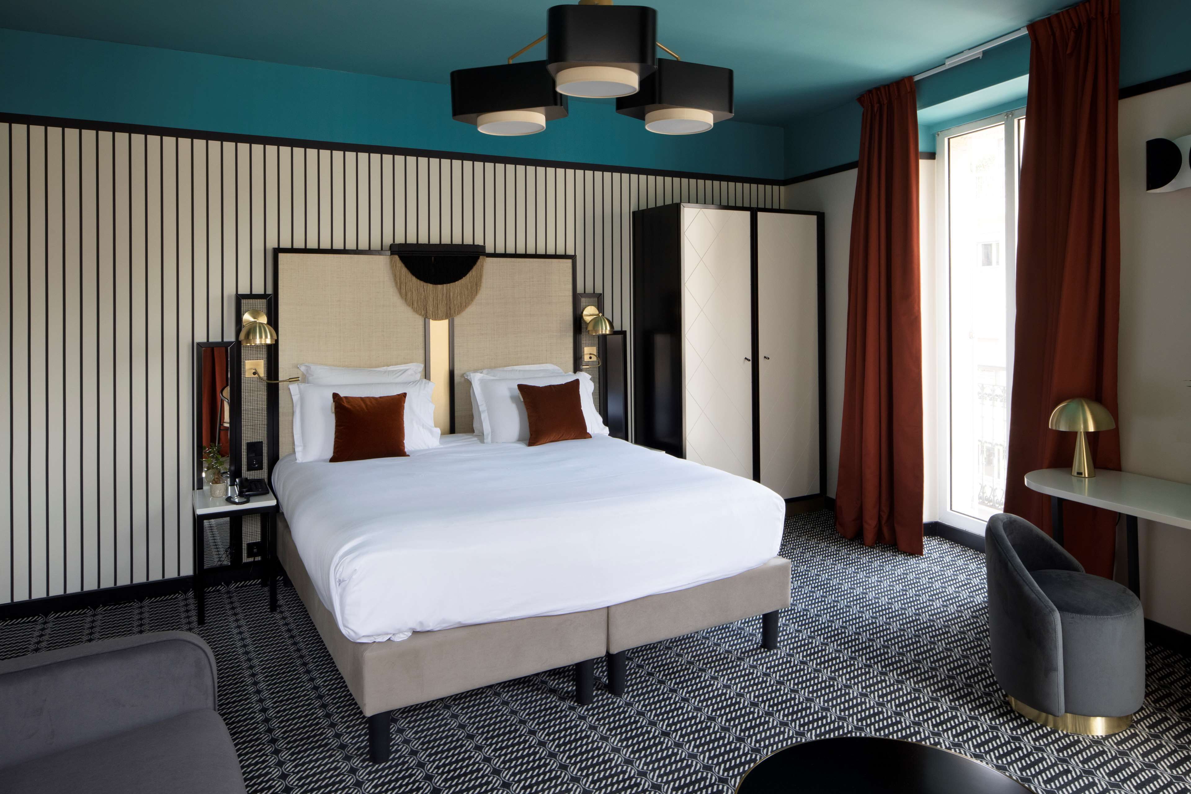 Une chambre d’hôtel avec un grand lit, un bureau, une chaise, une armoire et une fenêtre avec des rideaux.