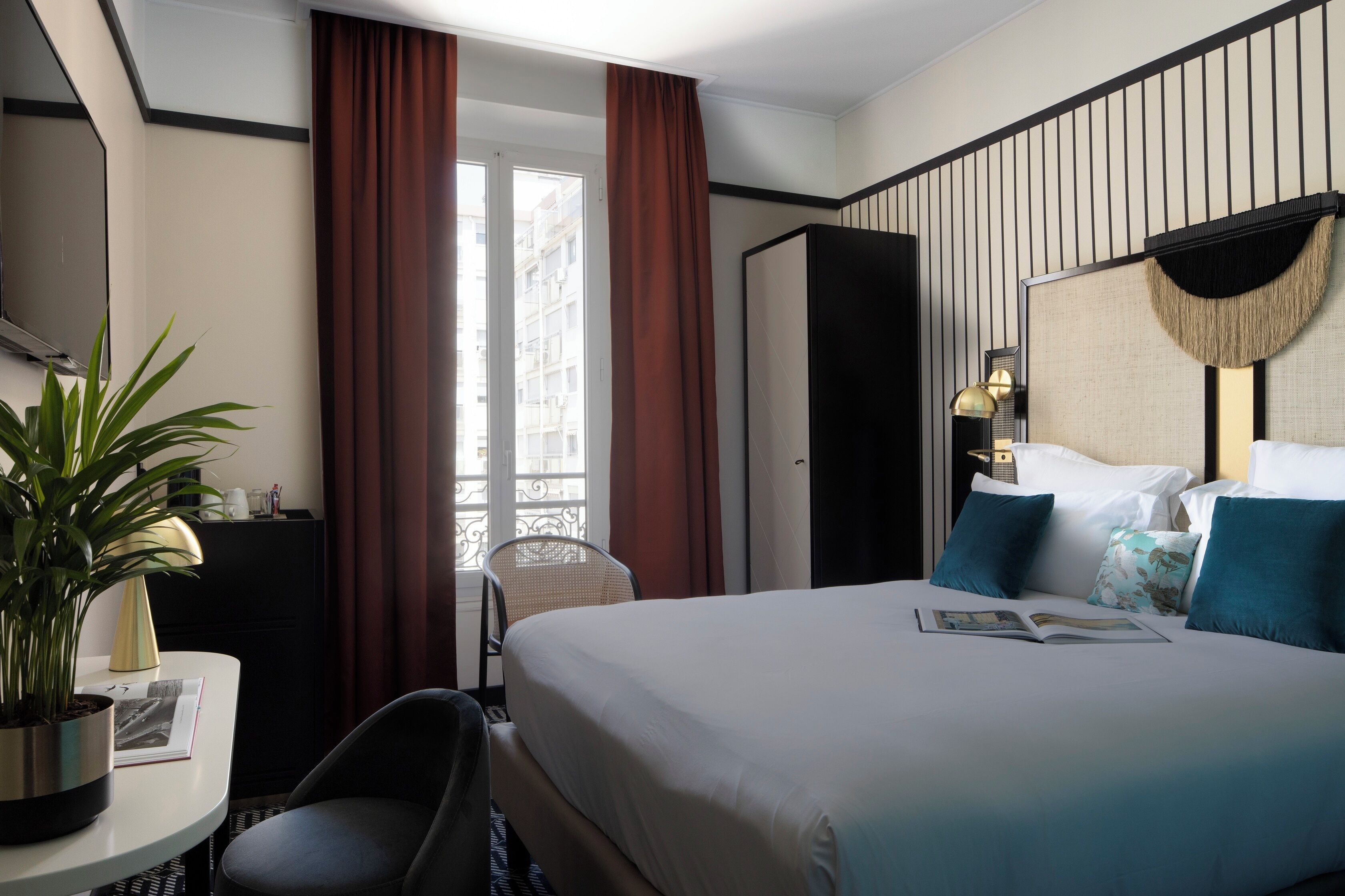 Habitación de hotel con una cama, una silla, una mesa con una planta, una lámpara y vistas al exterior.