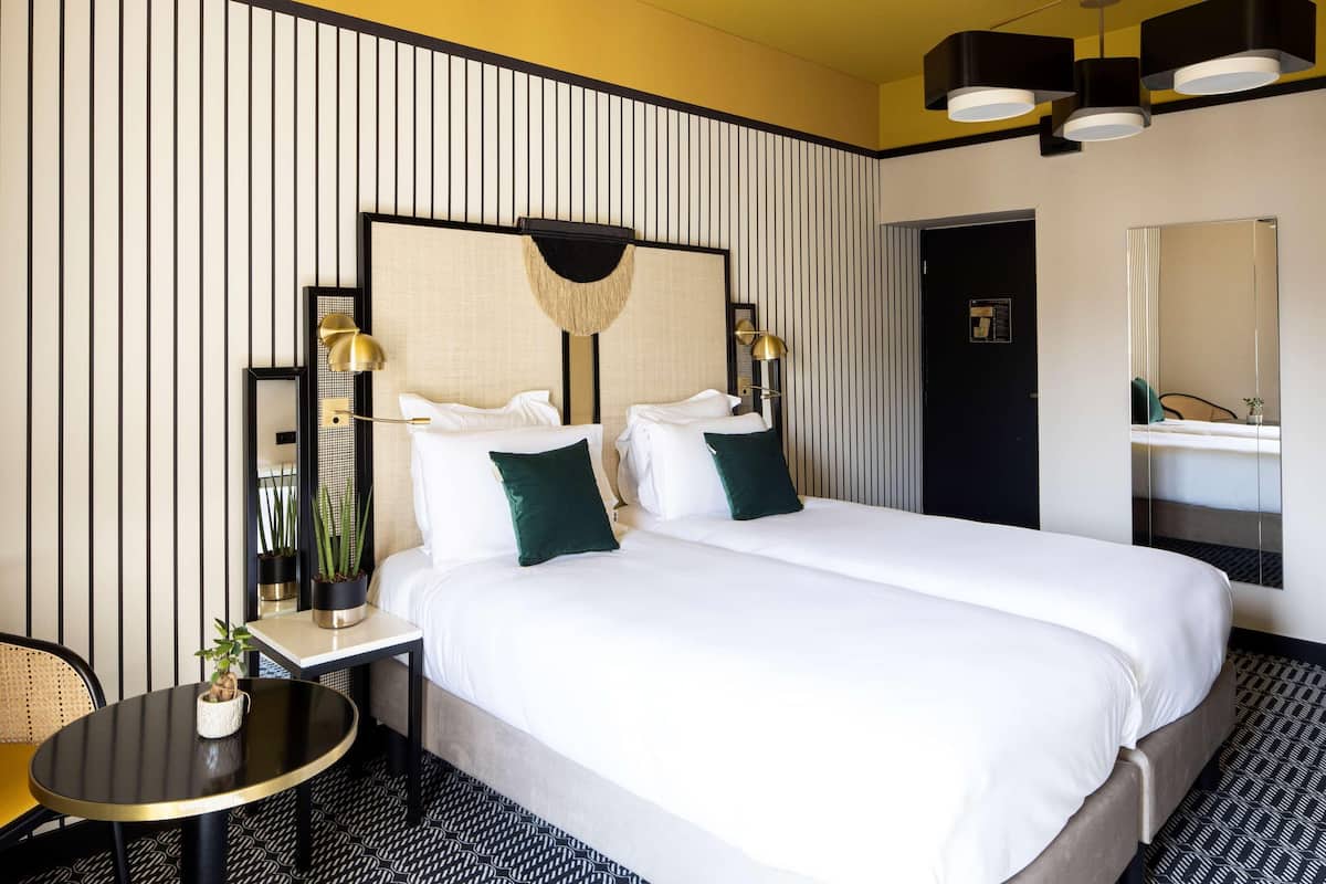 A hotel room with a large bed, two bedside tables, a round table, a chair, a mirror, and a door.