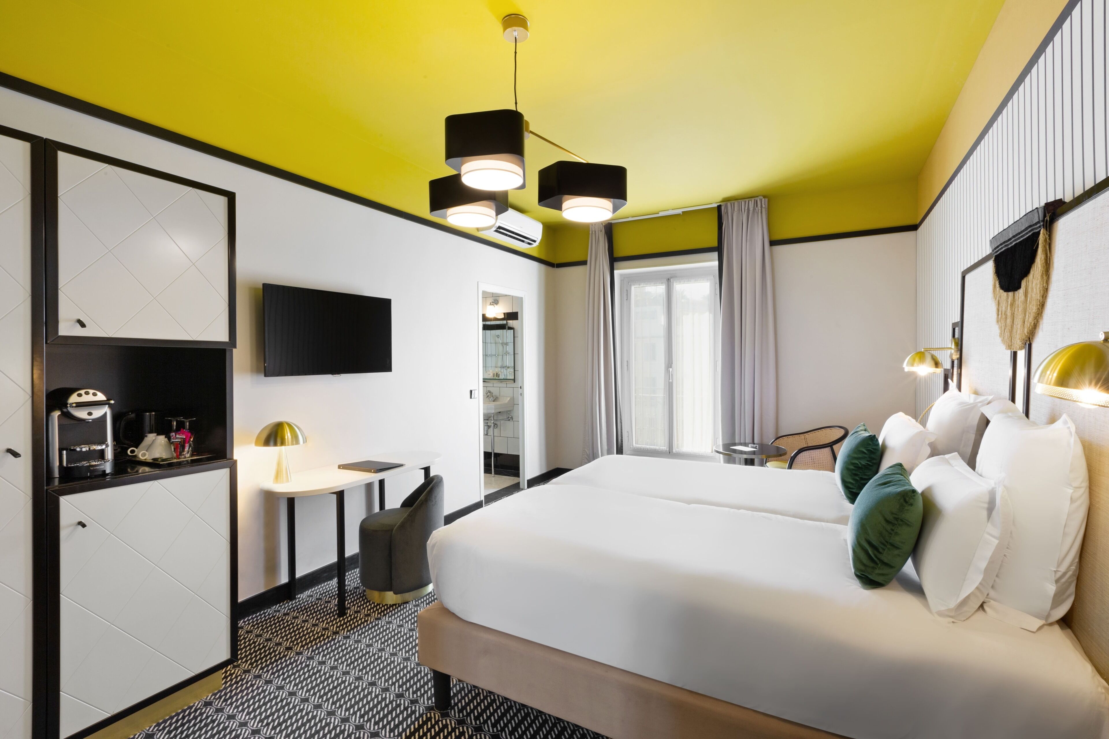 Una habitación de hotel con cama, mesita de noche, lámpara y televisión montada en la pared.