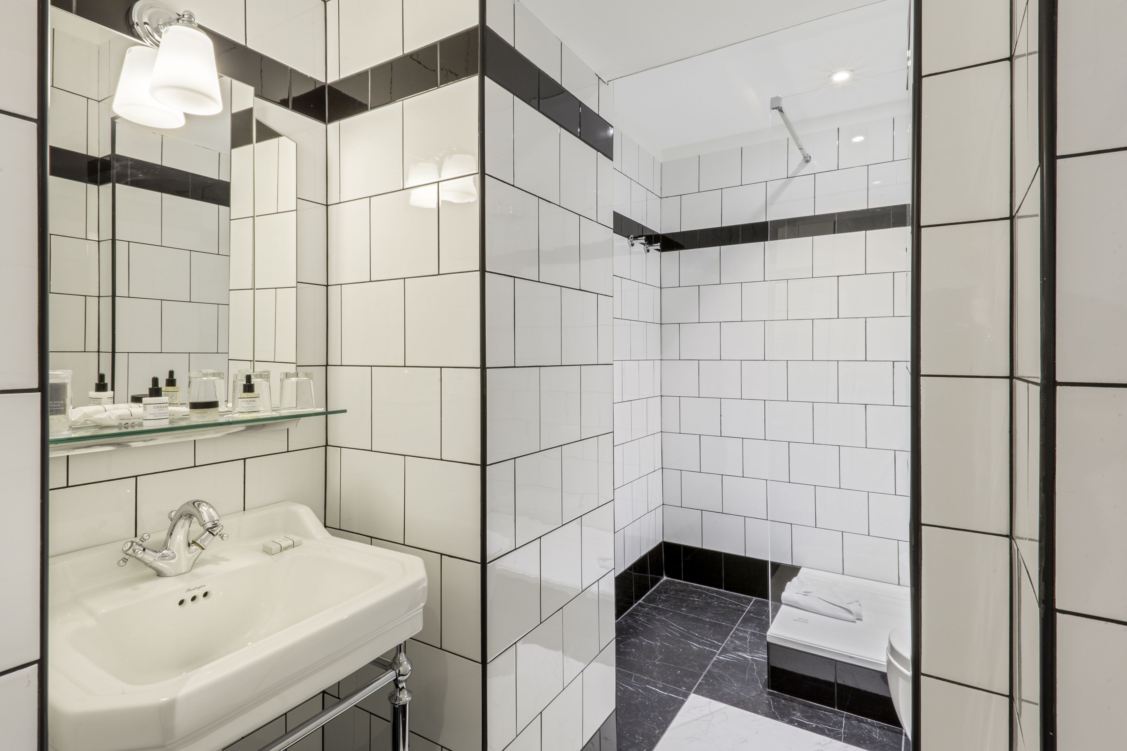 Um banheiro moderno com pia branca, prateleira de vidro e paredes com azulejos preta e branca.