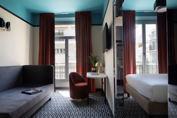 A hotel room with a sofa, a chair, a small table with a lamp, a bed, and a TV.