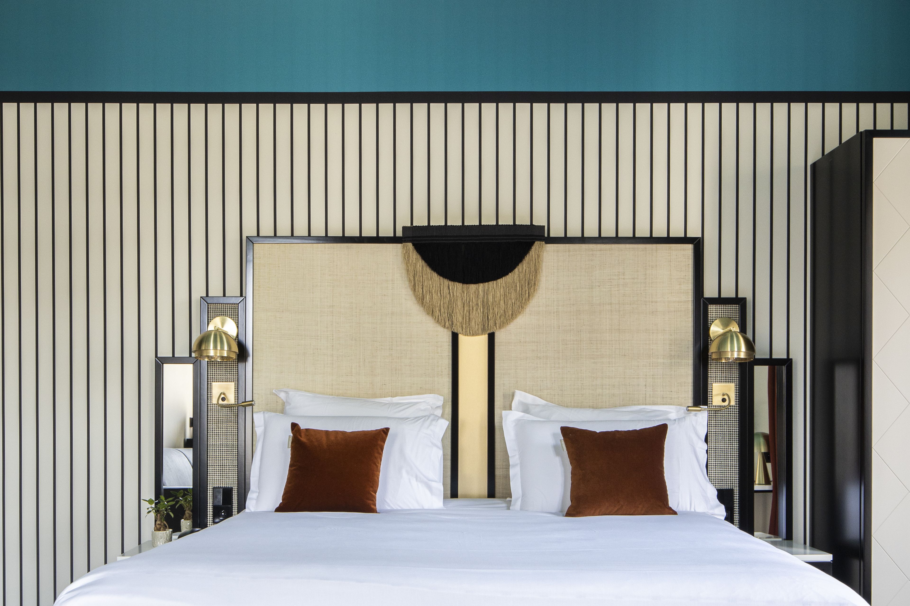 A hotel room with a large bed, two bedside tables with lamps, a wall-mounted mirror, and a textured headboard.