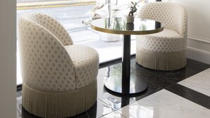 A modern interior with two patterned armchairs, a round table, and a view of a street with a 'Twinset' store. - Best Western Premier Hotel Roosevelt (Nice)