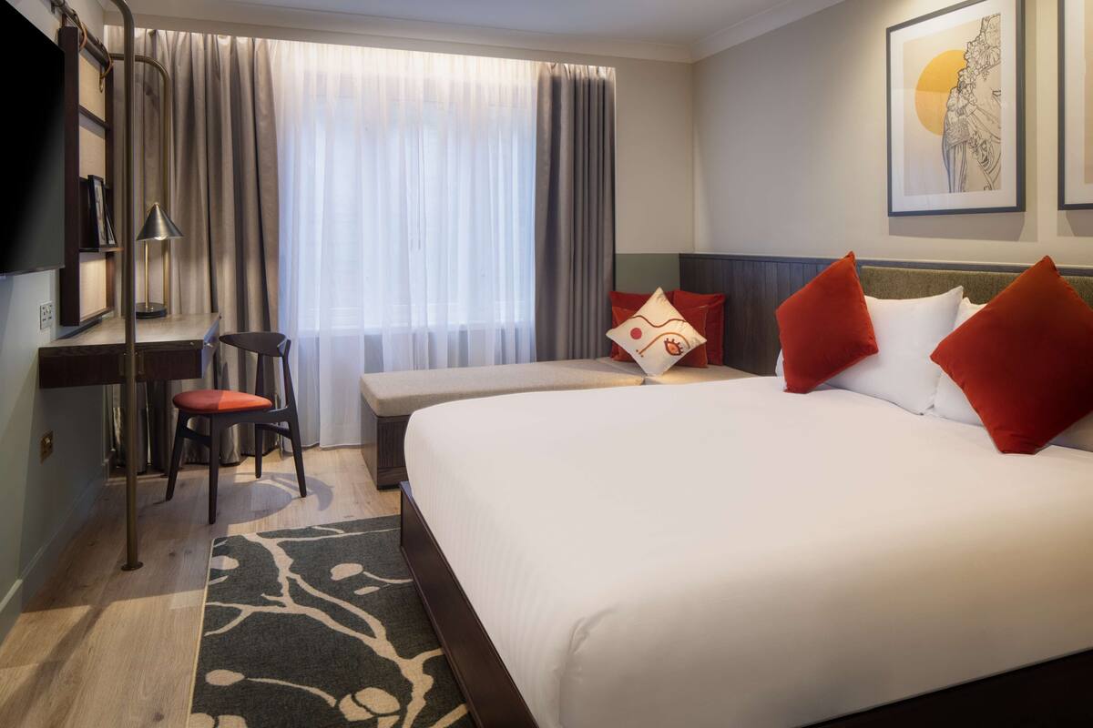A hotel room with a bed, a desk, a chair, a TV, and a window with curtains.
