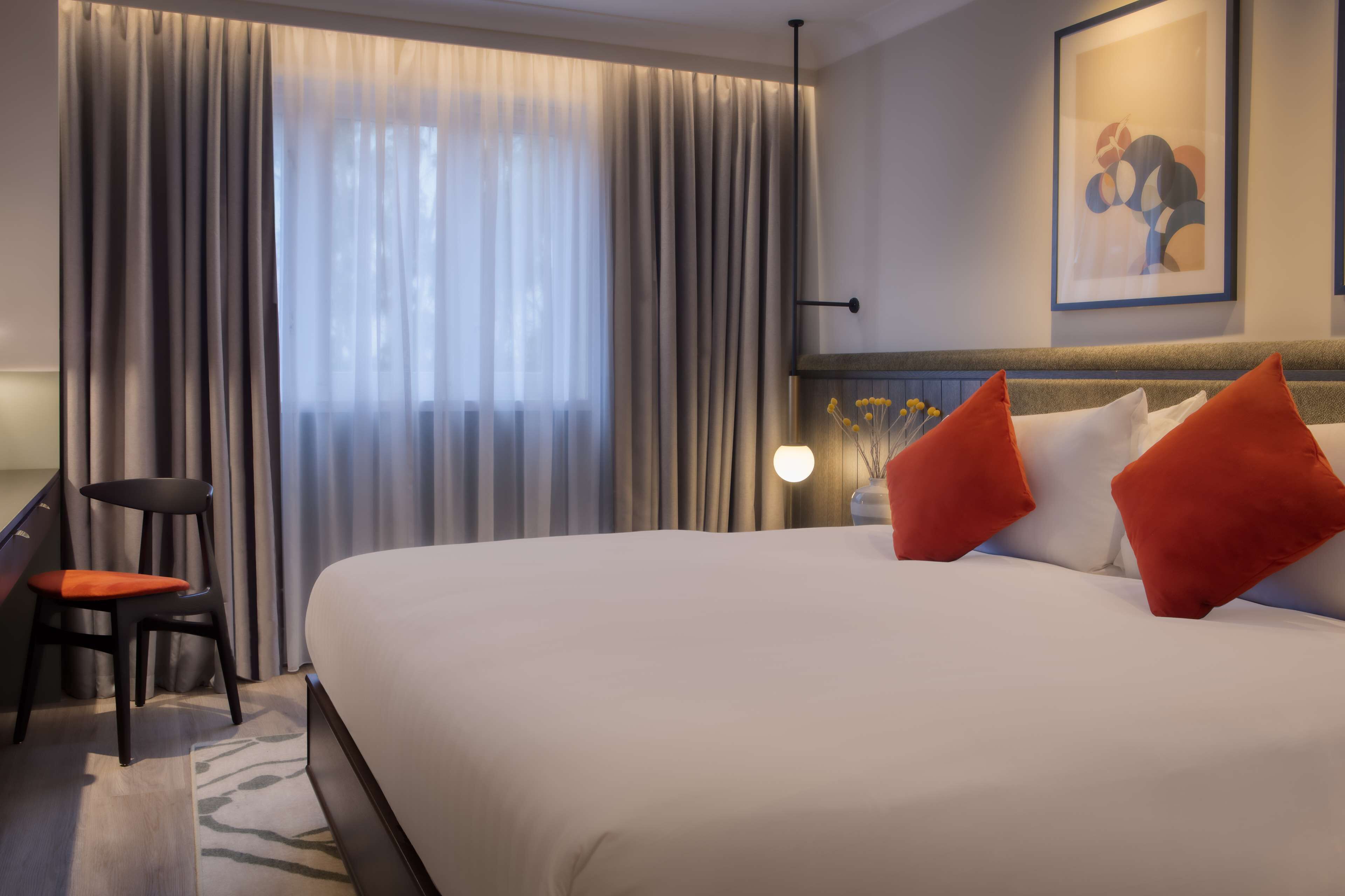 Habitación de hotel con una cama grande, un escritorio con silla, una lámpara y un cuadro en la pared.