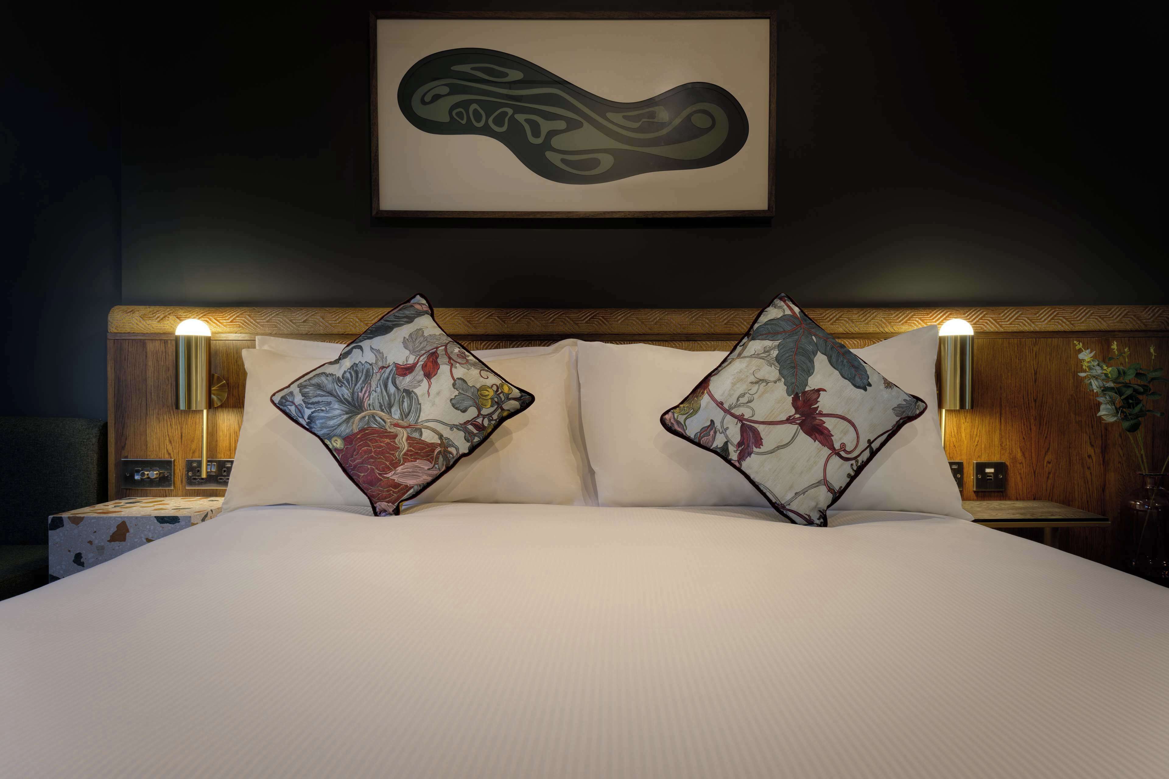 A neatly made bed with floral-patterned pillows and a framed artwork above.
