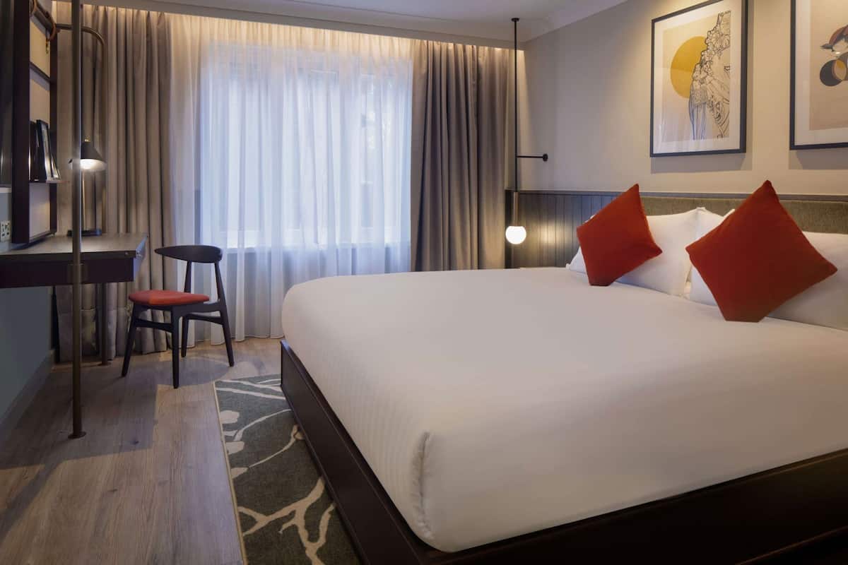 Hotellihuone, jossa on sänky, työpöytä, tuoli ja suuri ikkuna, jossa on verhot.