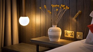 Ein Nachttisch mit einer Vase getrockneter Blumen, einer Wandleuchte und einer Steckdose.