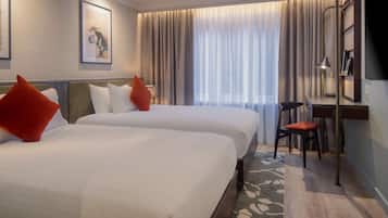 A hotel room with two beds, a desk, a chair, a TV, and a window with curtains.