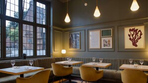 Ein Restaurantinneres mit Holztischen und gelben Stühlen, einer Sitzbank und Kunstwerken an den Wänden.