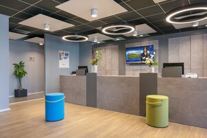 Un área de recepción con diseño moderno, que incluye un mostrador de recepción, una pantalla de televisión y una planta en maceta.