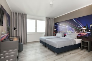 Una habitación de hotel moderna con una cama grande, un escritorio y un mural de la ciudad en la pared.