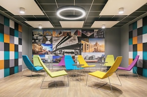 Un área de espera moderna con sillas de colores y un mural con vistas a la ciudad.