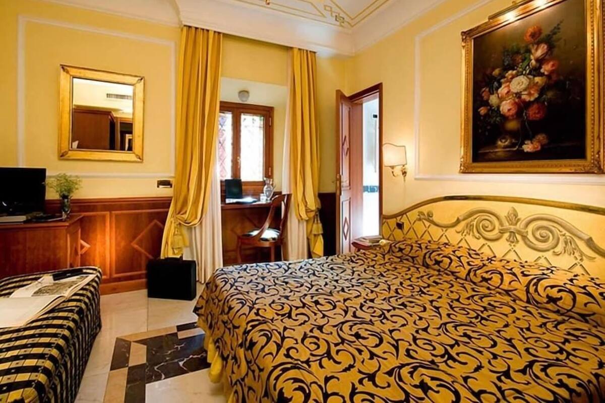 A hotel room with a bed, a desk, a chair, a television, and a painting on the wall.