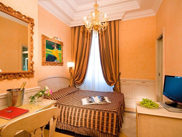A hotel room with a bed, a desk with a chair, a television, a chandelier, and a painting on the wall. - Comfort Hotel Bolivar (Rome)