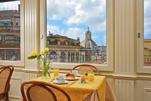 A dining table with breakfast items, a vase with flowers, and a view of a building with a dome through a window. - Comfort Hotel Bolivar (Rome)