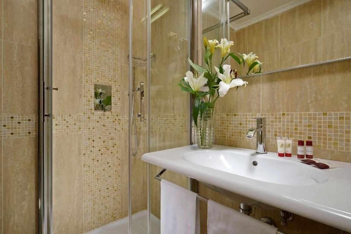 A bathroom with a glass shower enclosure, a white sink, and a vase with flowers.
