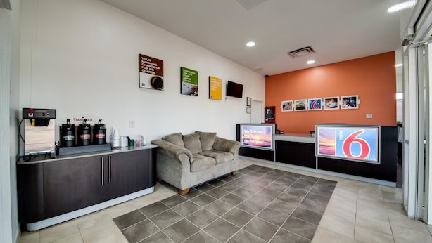 A hotel reception area with a sofa, a coffee machine, and a TV displaying the number 6. - Motel 6 Jennings, LA (Jennings)