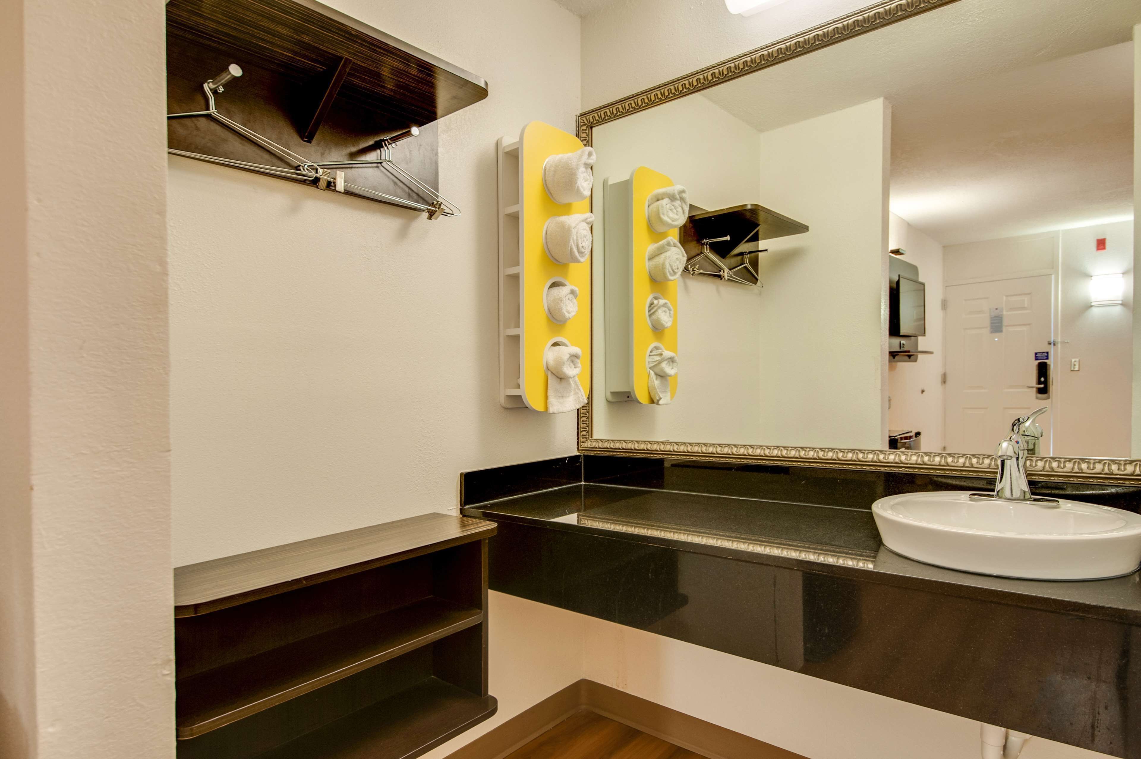 A bathroom with a black countertop, a white sink, and a mirror with a gold frame.