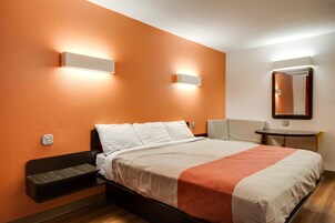 Habitación de hotel con cama, mesita de noche, una silla, una pequeña mesa y un espejo instalado en la pared.