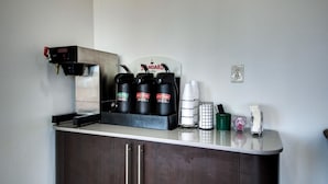 A kitchenette with a coffee machine, three coffee dispensers, a coffee cup holder, and a small trash bin. - Motel 6 Jennings, LA (Jennings)