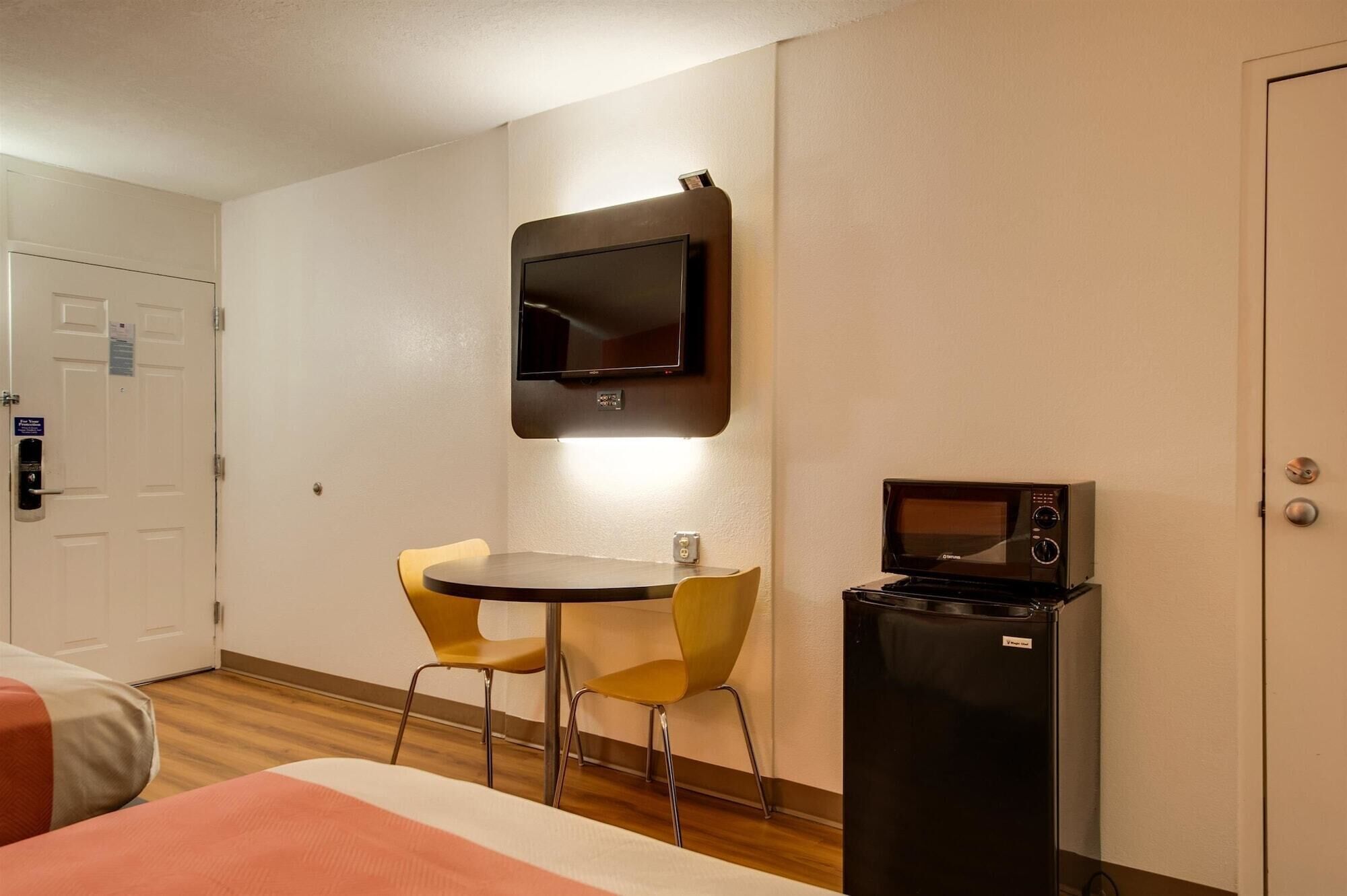 Habitación de hotel con cama, escritorio con dos sillas, televisor montado en la pared y microondas sobre una mesita.