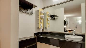 A modern bathroom with a large mirror, a white sink, and towel hooks.