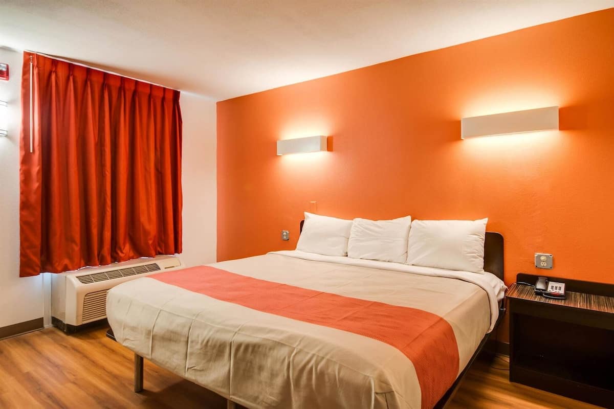 Una habitación de hotel con cama, aire acondicionado, mesita de noche y teléfono en la pared.