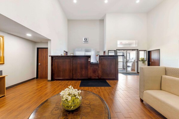 Un vestíbulo de hotel con mostrador de recepción, un sofá, suelo de madera y un jarrón con flores.
