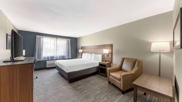 A hotel room with a bed, a desk, a chair, a lamp, and a bedside table.