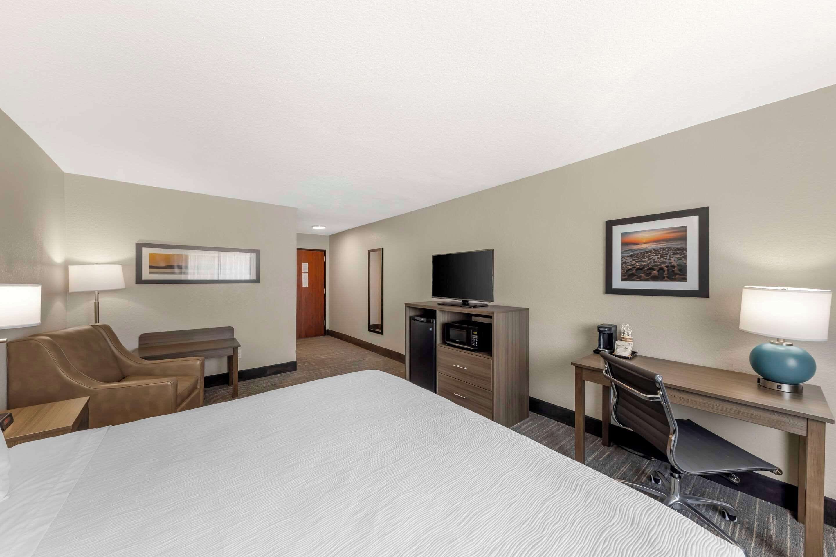 Habitación de hotel con una cama grande, un escritorio, una silla, un televisor, un microondas y una lámpara.