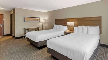 A hotel room with two beds, a desk, a chair, and a lamp.
