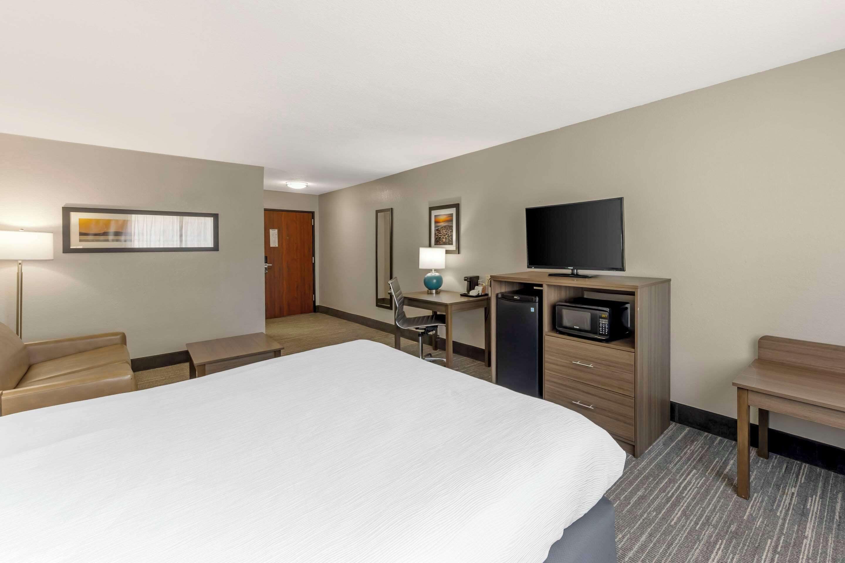 Una habitación de hotel con una cama grande, un escritorio con computadora, televisor y microondas.