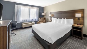 A hotel room with a large bed, a desk, a chair, a TV, and a window with curtains. - Quality Inn El Reno (El Reno)