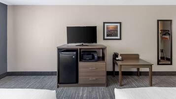Une chambre d’hôtel comprenant un lit, un bureau avec un micro-ondes, une télévision et un petit placard.