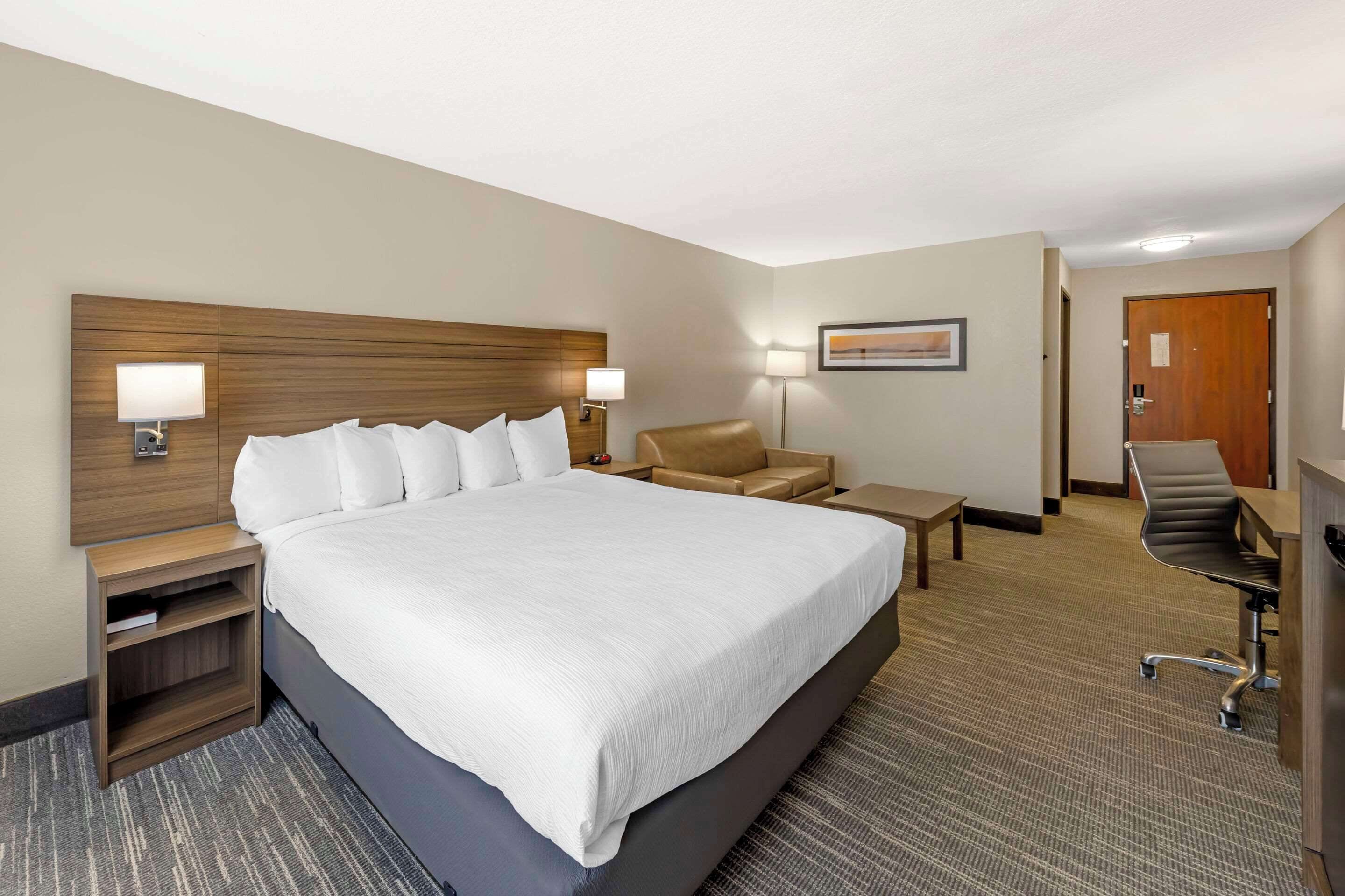 A hotel room with a large bed, a desk, a chair, and a nightstand.