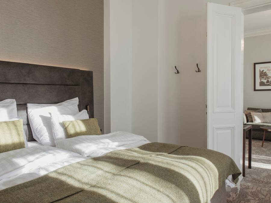 A neatly made bed with a headboard, a white door, and a framed picture on the wall.