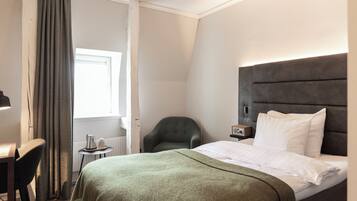 Una habitación de hotel con una cama, una silla, una mesita y una ventana con cortinas.