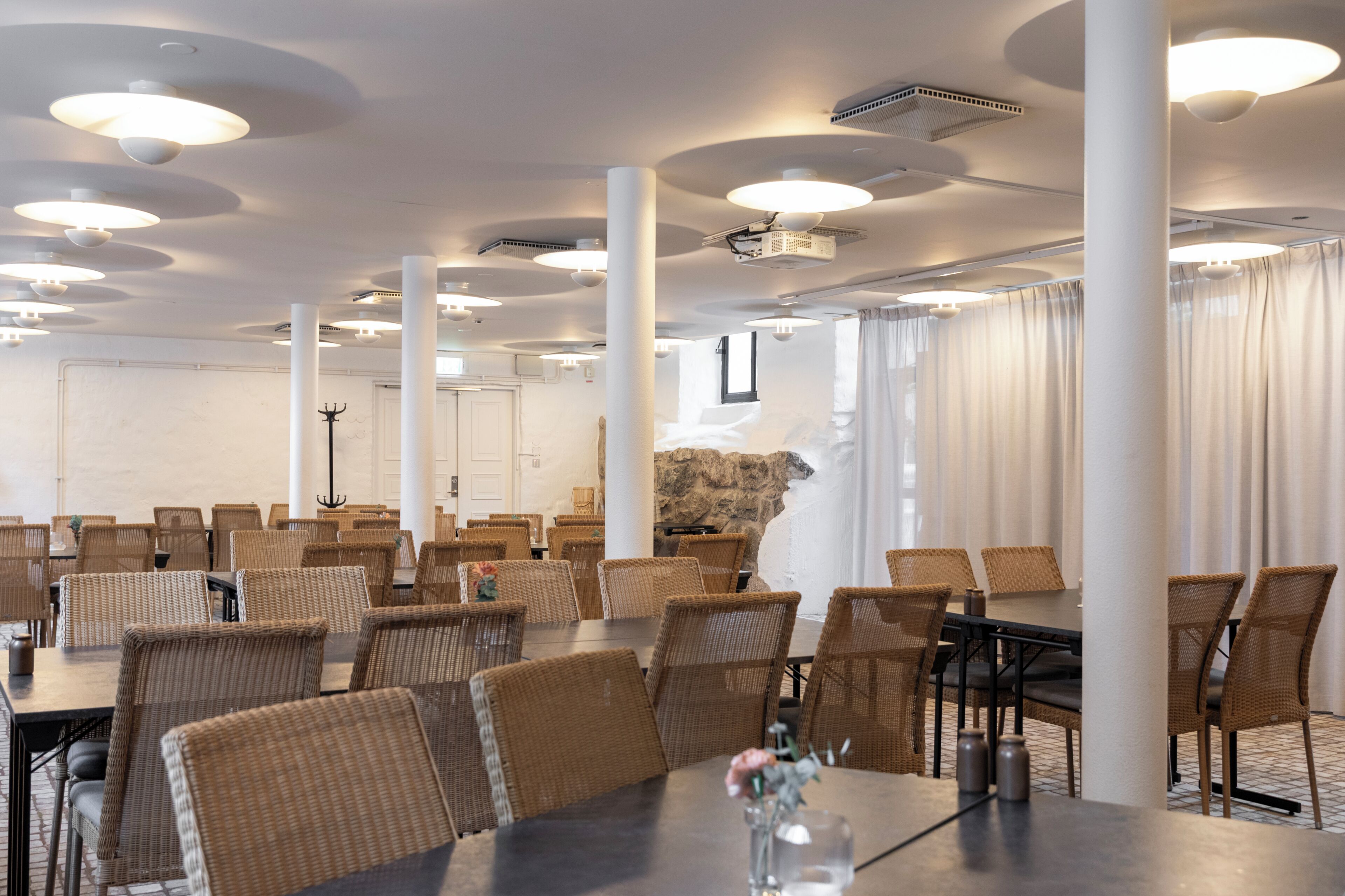 A conference room with round tables and chairs, white pillars, and a stone wall.