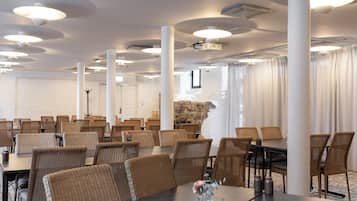 A conference room with round tables and chairs, white pillars, and a stone wall.