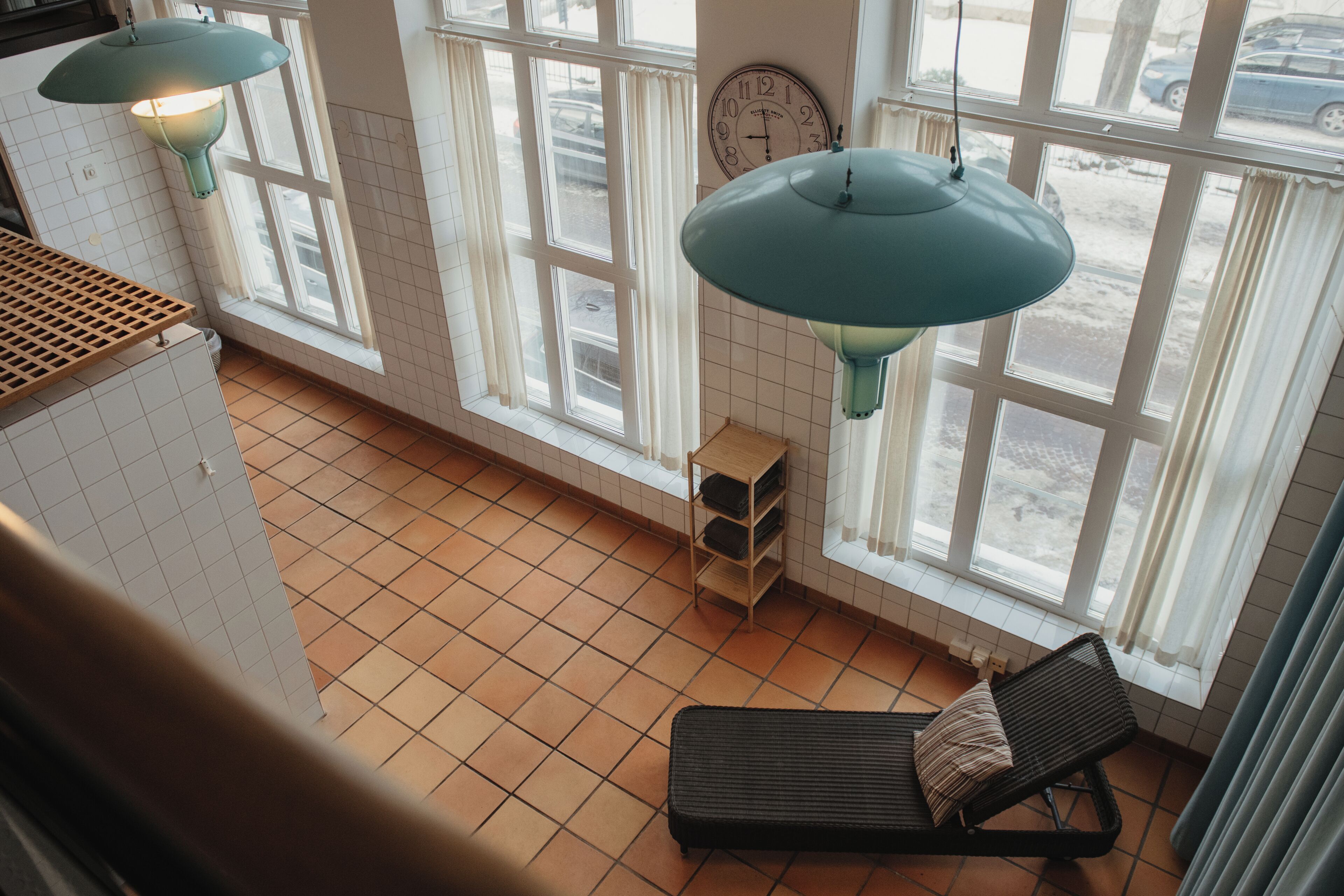 A room with large windows, a clock, a bench, and hanging lamps.