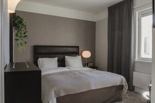 Habitación de hotel ordenada con cama, mesita de noche, lámpara y ventana con cortinas.